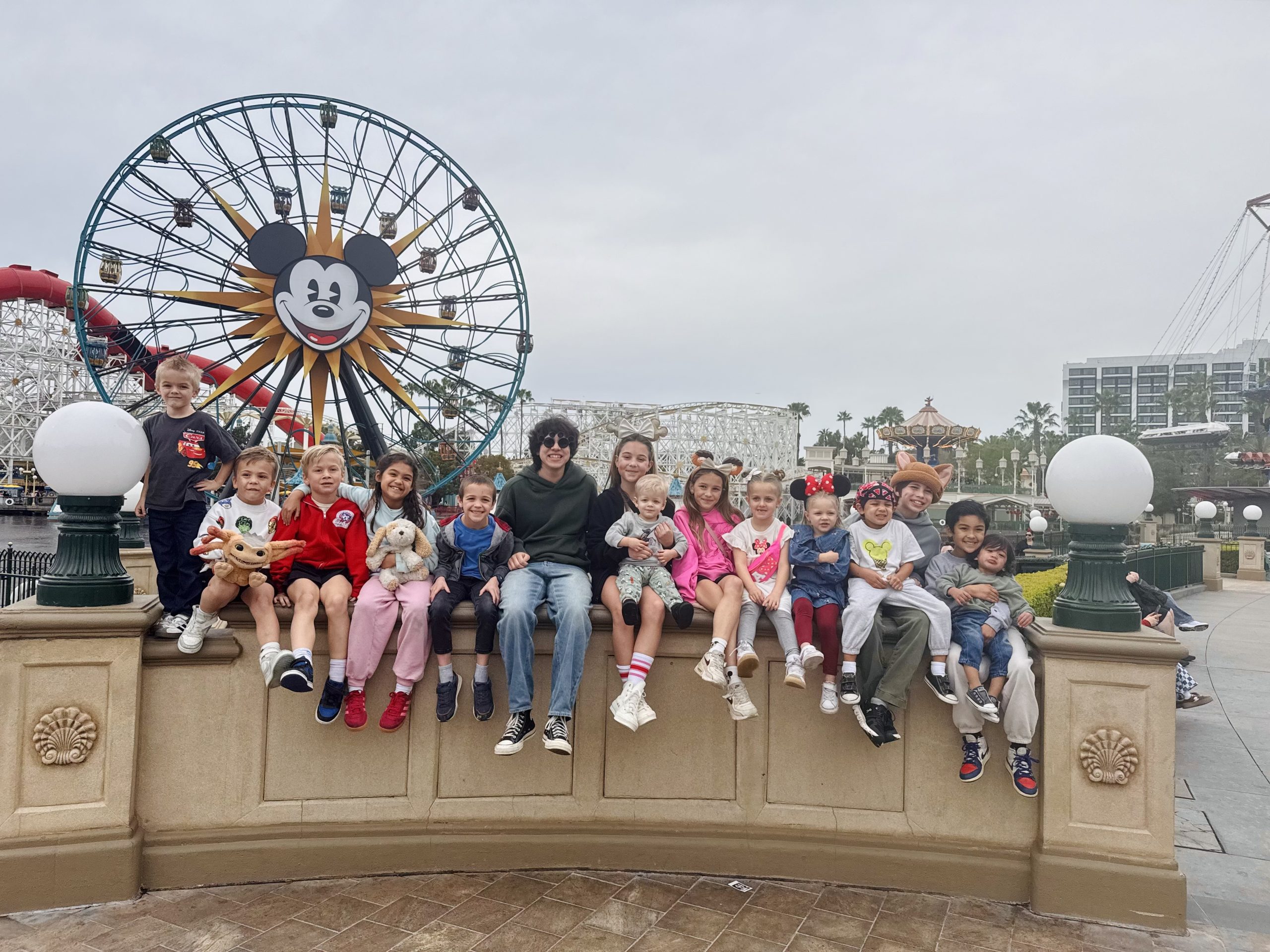 Adelaide's kids, nieces, and nephews are sitting together in front of the Mickey ferris wheel at Disneyland.
